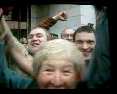 Screen mostly filled with four people's faces smiling, arms waving in air
