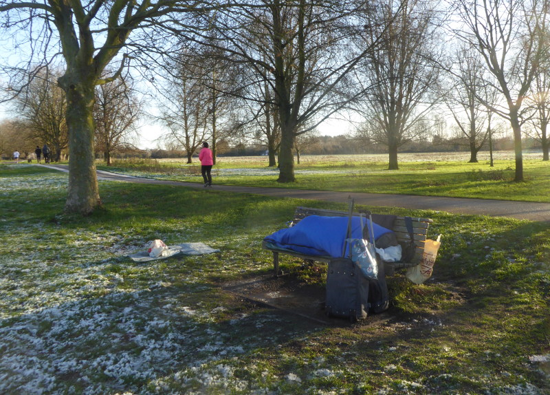 28 December 2017, 10:00am: A man in a sleeping bag on a bench on Stourbridge Common, Cambridge, white frost on the ground.