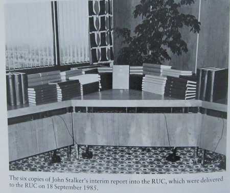 Dozens of thick volumes stacked on office desks with a large indoor plant on the floor behind.